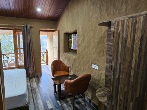 een slaapkamer met een bed, een tafel en stoelen bij Basho Mud Huts in Bashist