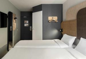 a bedroom with two white beds and a door at B&B HOTEL Toulouse Cité de l'Espace Hurel in Toulouse