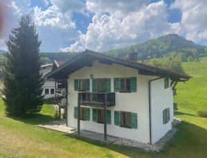 a white house with green shuttered windows in a field at Landhaus Maiergschwendt inkl Chiemgaukarte in Ruhpolding