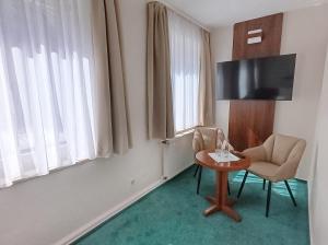 a room with a table and a chair and a television at REGIOHOTEL Bunte Stadt in Wernigerode