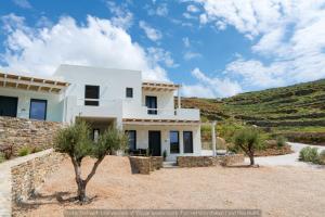 a white house with trees in front of a hill at Rockaine Suites Echoes in Tinos