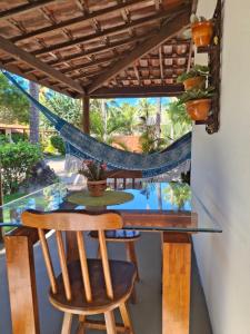 a glass table with chairs and a hammock on a patio at Recanto Verde - Praia de Santo Antônio in Diogo