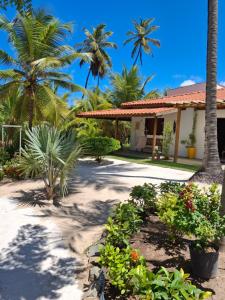a house with palm trees and flowers in front of it at Recanto Verde - Praia de Santo Antônio in Diogo