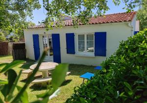 une petite maison blanche avec des portes bleues et une table de pique-nique dans l'établissement Les Cariatides, à La Cotinière