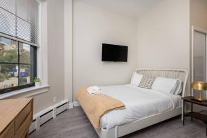 a white bedroom with a bed and a tv on the wall at Lovely South End Studio in Boston