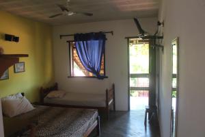 a bedroom with a bed and a window with blue curtains at Pousada Arco Íris in Conceição da Barra