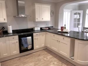 una cucina con mobili bianchi e ripiani neri di Pen Y Frith Bungalow a Prestatyn
