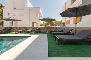 a pool with chairs and umbrellas next to a building at Villa Pagus with pool and private parking in Novalja