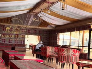 a man sitting at a table in a room with red chairs at Manar Bubble Luxury Camp in Wadi Rum