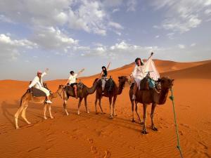 four people riding on camels in the desert at Sunset Sahara Luxury Camp in Merzouga