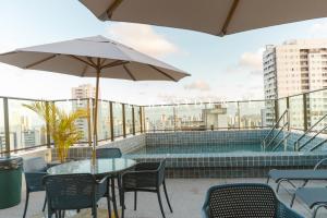 a patio with a table and chairs and an umbrella at Flat LUXO Boa Viagem Allure 1305 com piscina in Recife