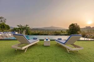 2 Stühle und ein Tisch neben einem Pool in der Unterkunft SaffronStays Euphoria in Dhamni