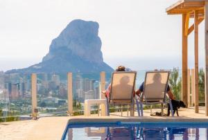 two people sitting in chairs by a pool with a mountain at Ons Spanje in Calpe