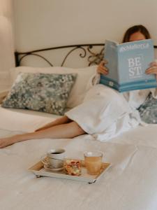 a woman laying on a bed reading a book with cups and a tray of food at Son Sant Jordi in Pollença