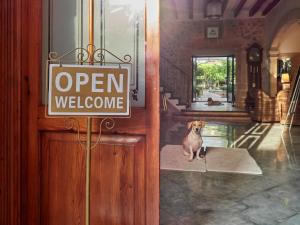 a dog sitting in front of a door with a open welcome sign at Son Sant Jordi in Pollença