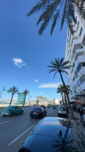 Una calle con coches y palmeras y un edificio. en Appartement Bord de Mer, en Tánger 12 fotos más