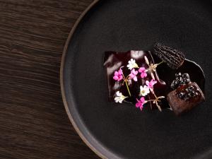 a black plate with a chocolate dessert with flowers on it at Hotel Arctic in Ilulissat