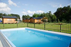 a swimming pool in front of a fence with houses at Domki z basenem & kajaki u Krysi in Borne Sulinowo