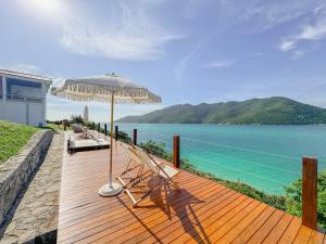 a wooden deck with an umbrella and chairs and the ocean at Hotel Recanto do Atalaia in Arraial do Cabo