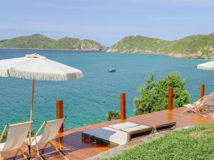 a wooden deck with an umbrella and chairs and the water at Hotel Recanto do Atalaia in Arraial do Cabo