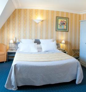 a bedroom with a large bed with white pillows at Logis Hotel Du Casino Restaurant Le Mathelia in Vierville-sur-Mer