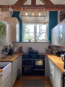 eine Küche mit weißen Schränken und einem schwarzen Herd mit Backofen in der Unterkunft St Catherines Cottage The Old Schoolhouse in Long Melford