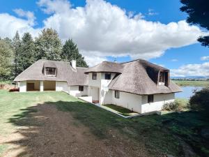 a house with a thatched roof on a grass field at Rivermead in Himeville