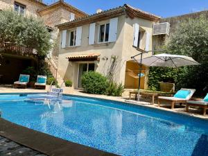 a swimming pool with chairs and an umbrella next to a house at Gîte familial 6 personnes climatisé, piscine partagée chauffée, proche Nîmes, Uzès, Pont du Gard, Cévennes in Saint-Géniès-de-Malgoirès