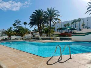 een zwembad met palmbomen en een gebouw bij Cozy Apartament Maspalomas in San Bartolomé