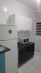 La cuisine est équipée d'un réfrigérateur blanc et d'un four micro-ondes. dans l'établissement Casa na Praia Grande, à Praia Grande