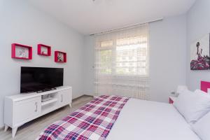 a white bedroom with a bed and a tv at Апартамент Веирас 2 in Velingrad