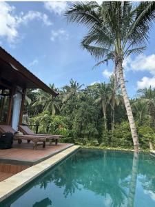 a swimming pool next to a house with a palm tree at Villa Pondok Utu, Ubud - Bali in Ubud