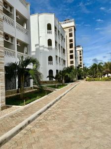 a large white building with palm trees in front of it at Azar Stays Diani in Diani Beach