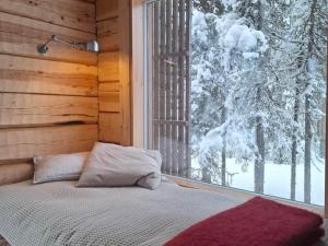 un letto in una camera con finestra e alberi innevati di Handcrafted Log Chalet Villa Aarreaitta a Pudasjärvi
