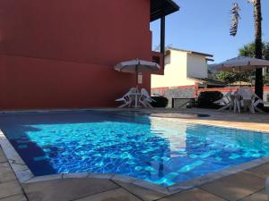 a swimming pool with chairs and umbrellas next to a building at Apartamento Duplex em Juquehy in São Sebastião