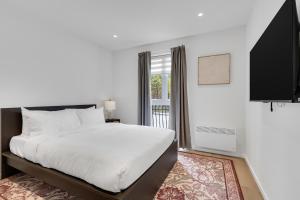 a white bedroom with a bed and a window at Le Victoria Midtown Mtl in Montréal