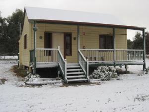 Una pequeña casa amarilla con un porche en la nieve. en Drovers Retreat, en Thulimbah