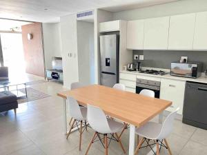 a kitchen with a wooden table and white chairs at 2 Bedroom combo with pool at Ocean Dune, Sibaya in Umdloti