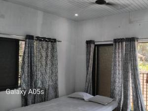 a bedroom with curtains and a bed and a window at VAIBHAV NAIk MADHULI COTTAGE in Alībāg