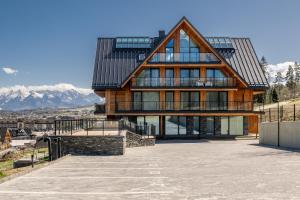 a large wooden house with mountains in the background at TatryTop Słoneczna Rezydencja Jacuzzi & Sauna in Białka Tatrzanska
