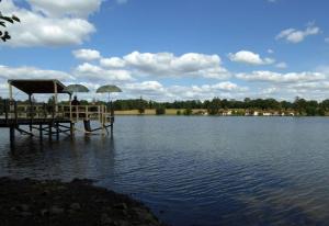 zwei Personen sitzen mit Sonnenschirmen auf einem Steg an einem See in der Unterkunft La petite maison de l'étang in Magnac-Laval