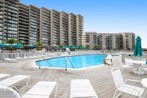a swimming pool with white chairs and a large building at Sea Colony - 17001 Bayberry in Bethany Beach