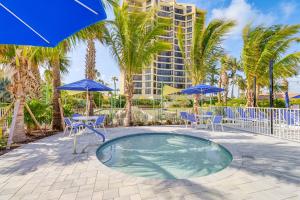 a pool with chairs and blue umbrellas and a building at Luxe Fort Pierce Beach Condo with Golf Views! in Fort Pierce