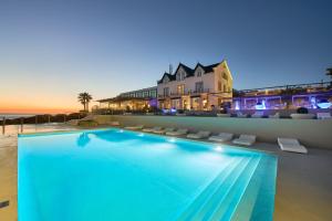 a swimming pool in front of a house and the ocean at Farol Hotel in Cascais