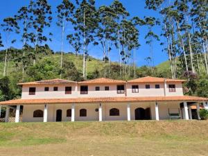 a large white house with trees in the background at Sitio Longos Vales in Miguel Pereira