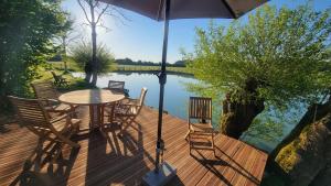 eine Holzterrasse mit einem Tisch und Stühlen neben dem Wasser in der Unterkunft La Gravardière, Nature & Pêche, 5min de la ville in Belhomert-Guéhouville