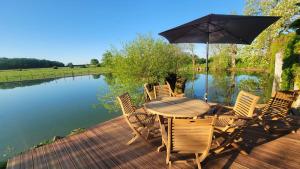 a wooden table with chairs and an umbrella next to a pond at La Gravardière, Nature & Pêche, à 5min de la ville in Belhomert-Guéhouville