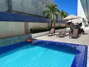 una piscina con sillas, mesa y sombrilla en Bela Hospedagem - Imperial Flat - Beira mar de Tambaú, en João Pessoa