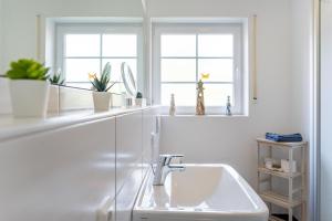 een witte badkamer met een wastafel en 2 ramen bij Ruhepol in Greetsiel +33 foto's