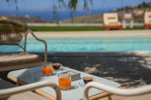 two glasses of orange juice on a table next to a pool at Oliva Emerald Eco - Secluded Off-Grid Vineyard Villa in Káto Váthia
